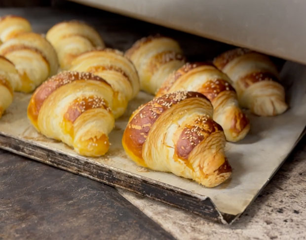 Ein Blech mit goldbraunen Croissants, frisch aus dem Ofen, bestreut mit Sesam, auf Backpapier liegend.